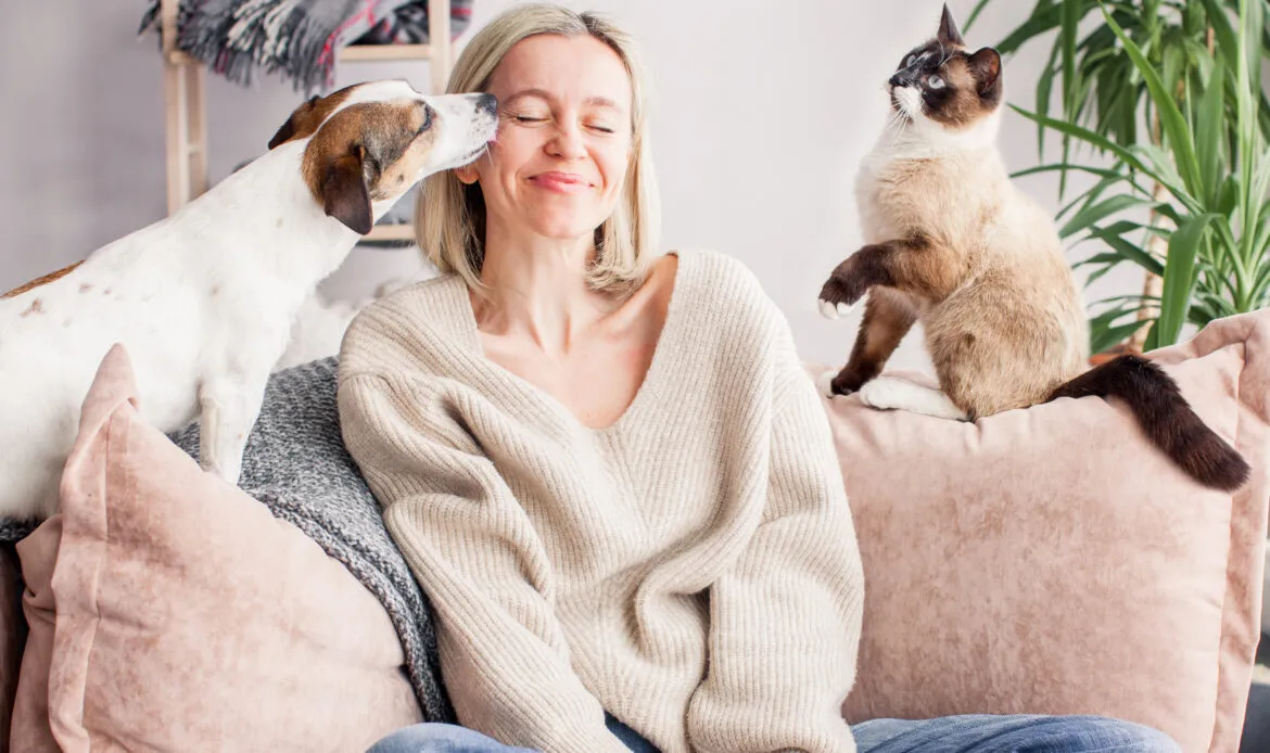 Happy woman resting on a couch with her dog and a cat