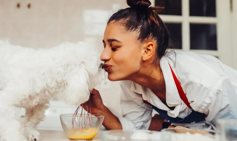 Woman and her dog kissing while she bakes.
